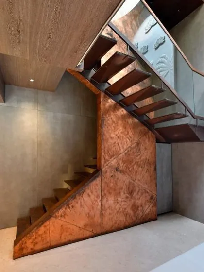 This sculptural staircase is a centerpiece, crafted from copper and metal with cantilevered wooden treads. It embodies a dialogue between lightness and intensity, transforming the act of ascent into a sensory experience, complemented by the natural light from a circular skylight above.
