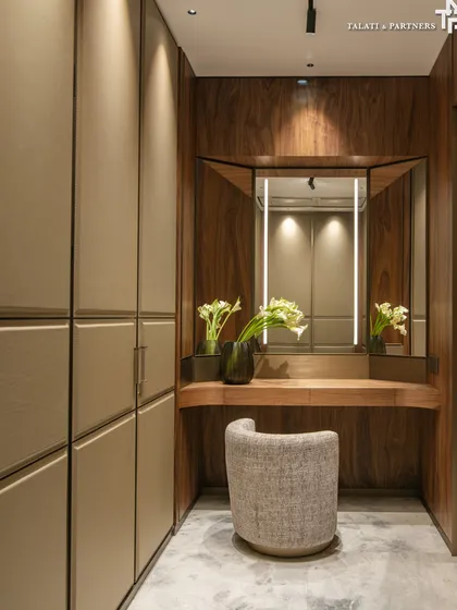 A walk-in dressing space that is a study in quiet luxury. Rich, dark-toned wood with pronounced veins brings warmth and depth, layered with soft neutrals in browns and beiges. Polished marble floors and a simple, elegant vanity complete the look.