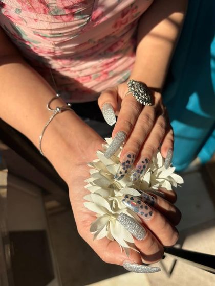 A striking combination of silver glitter and black heart-print nails on long, square extensions.