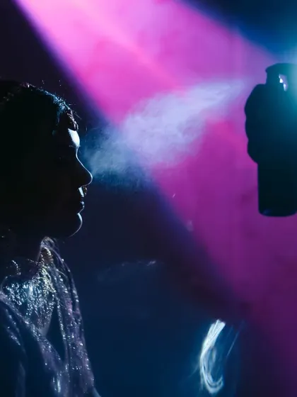 A creative, silhouetted shot of the final touches. The spray from the setting spray catches the light, creating a unique and artistic behind-the-scenes image.