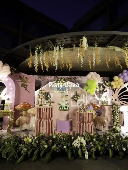 A full view of a fairy-themed stage setup at night. The lighting from the props and the hanging floral canopy above created a warm and magical glow over the entire area.