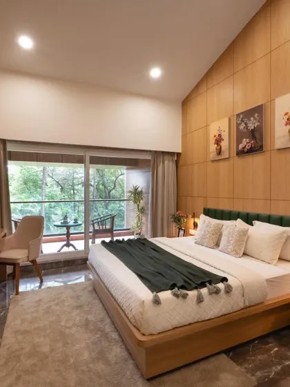 We design serene master suites that connect with the outdoors. This room features a custom wooden bed frame, a full-length wood-paneled accent wall, and sliding glass doors that open onto a private balcony with a lush, green view.