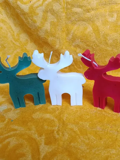 These reindeer-shaped candles in green, white, and red are a whimsical and fun decoration for the Christmas season.