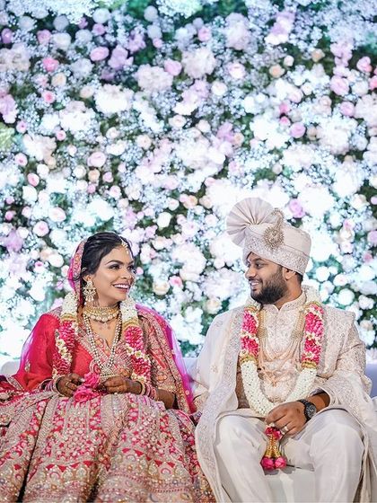 A beautiful shot of the couple seated against a wall of flowers after their jaimala, looking every bit the royal couple.