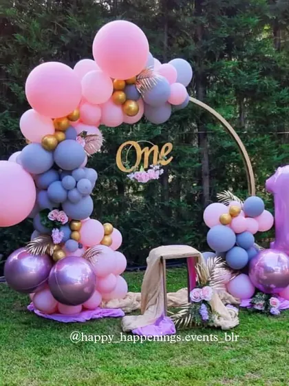 Celebrating a first trip around the sun. This beautiful outdoor setup for a first birthday features a lovely balloon arch in shades of pink and grey, with a golden "One" sign to mark the precious milestone.