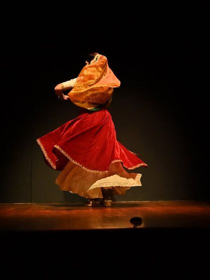 A solo spin captured in a moment of quiet intensity. The flowing red costume and veiled pose create a dramatic silhouette against the dark stage.