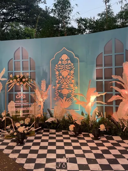 A custom photo booth designed with the Bar Palladio theme, featuring blue walls, intricate cut-out patterns, and paper palm trees.