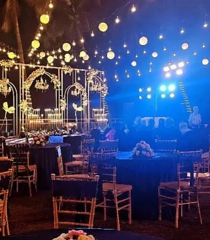 A glamorous Sangeet or reception setup with a dark blue and gold theme. The stage features intricate gold backdrops, and the guest tables are dressed in navy blue linens for a chic, cohesive look.