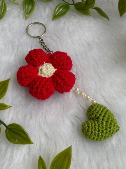 A close-up of the red flower and heart keychain, showing the texture of the petals and the delicate pearl accents.