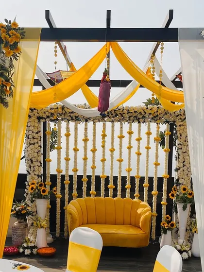 A complete view of a rooftop Haldi setup, featuring a floral-draped canopy, a comfortable seating area for the couple, and surrounding guest tables.