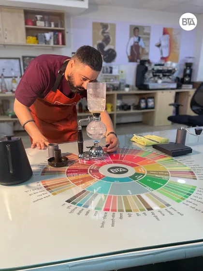 A trainer closely inspecting the Syphon brewing process. This method requires careful attention to temperature and timing to get it right.