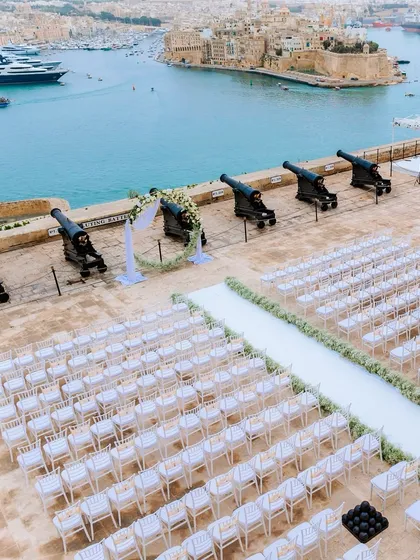 The Saluting Battery in Malta, transformed into a breathtaking wedding venue. The clean white aisle and chairs contrast beautifully with the historic cannons and the blue sea.
