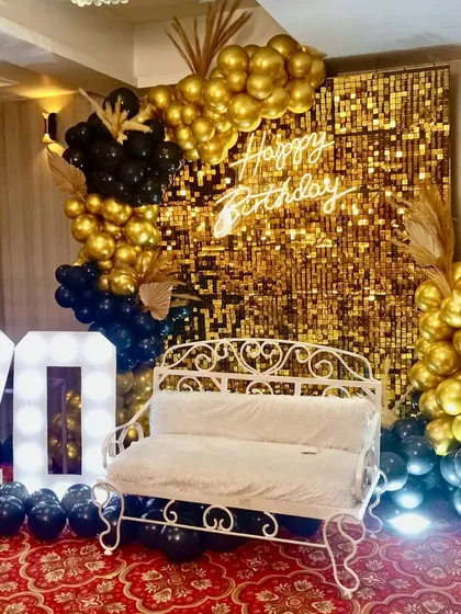 For a glamorous 70th birthday, we designed this stunning photo booth with a gold shimmer wall, a custom 'Happy Birthday' neon sign, and bold marquee numbers. The black and gold balloon arrangement adds a touch of sophisticated fun.
