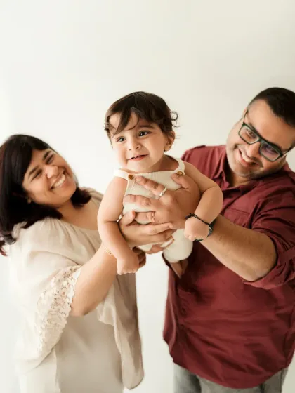 Parents playfully lift their smiling baby in the air. This action shot brings a sense of fun and energy to the family photoshoot.