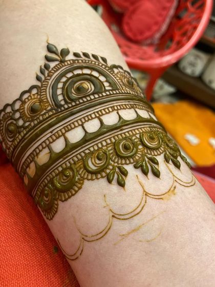 A close-up of a detailed henna cuff being applied, showing the clean outlines before filling.