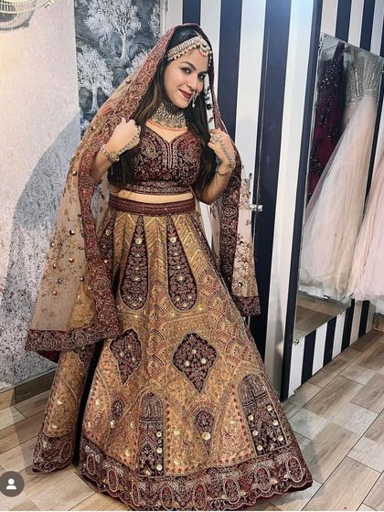 A happy client trying on a traditional maroon and gold bridal lehenga in our store. This shows the fit and fall of the outfit, perfect for a classic wedding look.