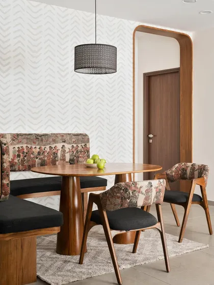 This cozy dining nook in our 'Palaash' project features a custom curved wall with built-in seating. The bold tribal-print upholstery is paired with a solid teak wood dining table.