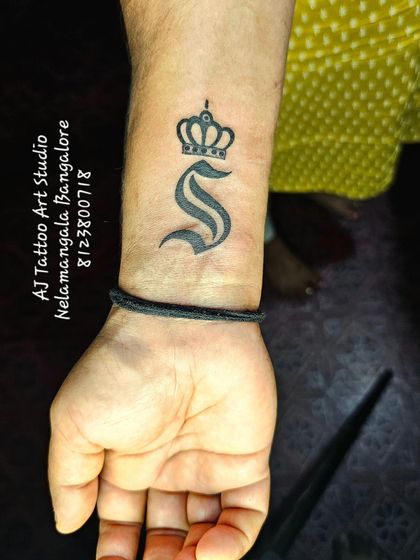 A bold initial 'S' with a crown on the wrist, a simple and royal design.