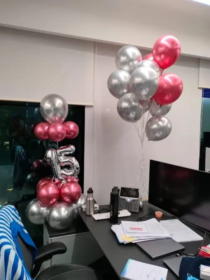 A surprise desk decoration for a 15th work anniversary or birthday. This includes a small balloon column with number foils and a separate bouquet of helium balloons in matching pink and silver.