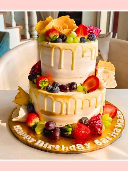 A fresh two-tier fruit drip cake, perfect for a sunny celebration, adorned with various fresh fruits.