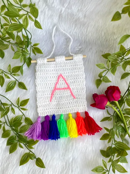 I make these personalized initial banners, perfect for a nursery or a child's room door. This one features the letter 'A' with a vibrant rainbow of tassels.