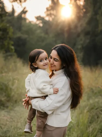 A mother holds her child as the sun sets behind them. The beautiful backlighting creates a warm and dreamy outdoor portrait.