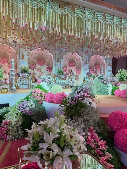 A view from the side, showing the lush, garden-like floral arrangements that line the stage. This creates a soft, romantic border for the grand mandap.