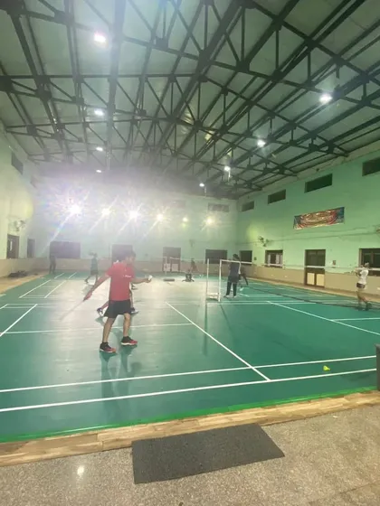 A wide-angle view of our well-lit indoor badminton hall during an evening session. We provide a professional environment for players to train in.