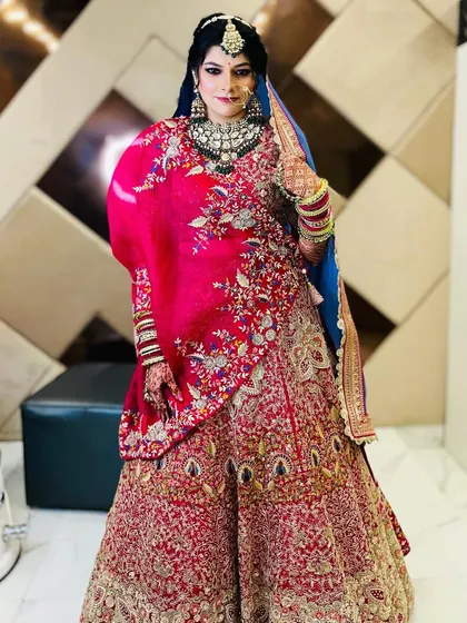 A full view of the bride in her red and blue lehenga, standing confidently in the salon. This shot captures the complete look in the context of where the magic happens.