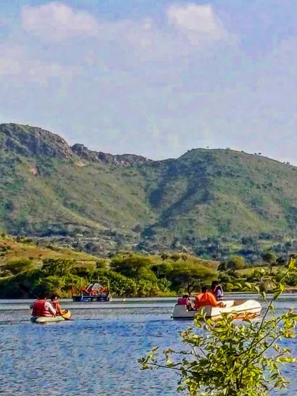 A scenic view of people kayaking and boating on a lake surrounded by the Aravalli hills in Udaipur. It's a relaxing way to spend the day and take in the stunning natural landscape.