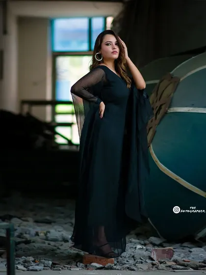 A full-length portrait from the industrial fashion shoot. The focus is on the model's pose and the elegant silhouette of the black dress against the rough background.