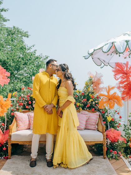 A sweet couple portrait in front of their colorful Haldi decor, capturing a quiet moment of affection amidst the celebration.