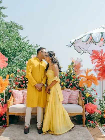 A sweet couple portrait in front of their colorful Haldi decor, capturing a quiet moment of affection amidst the celebration.