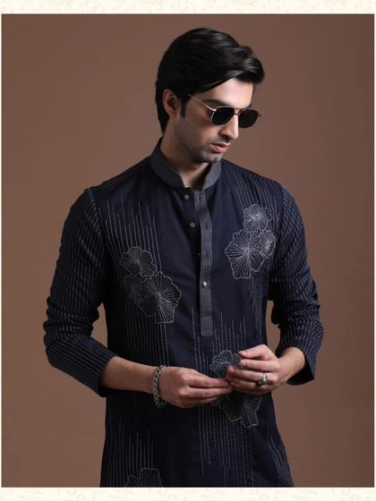 A close-up of a navy blue kurta with floral and linear embroidery. This piece is perfect for celebrating in style, with intricate detailing and impeccable tailoring.