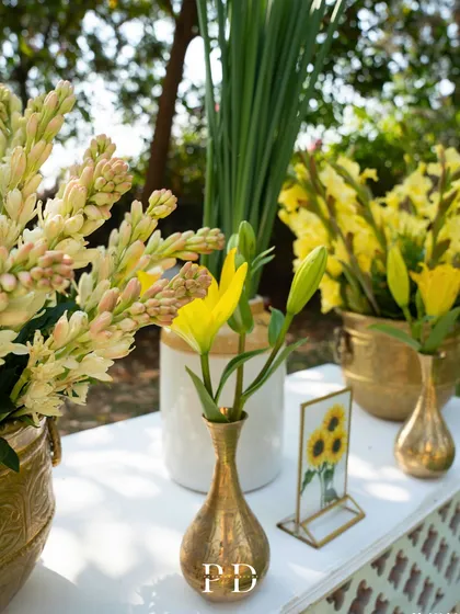 A detail shot of the Haldi decor, featuring fresh tuberoses and yellow flowers in brass vases, with a small framed sunflower print.