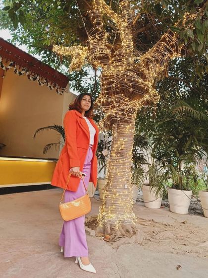 This full-length shot shows the complete color-blocked outfit. The bright orange coat and lavender pants create a stunning and fashion-forward combination, perfect for making an entrance.