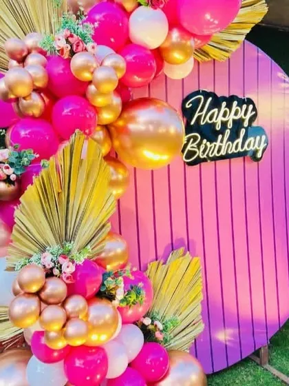 Another angle of the modern pink and gold birthday setup. This view shows how the balloon garlands are layered with floral elements to add texture and create a lush, celebratory photo corner.