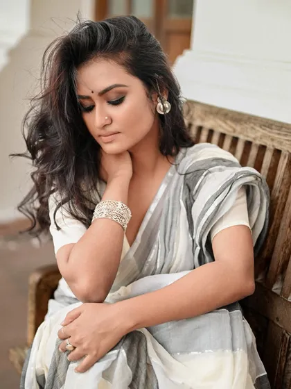 A thoughtful, seated portrait for AVA India. The model's relaxed pose on a wooden bench creates a relatable and gentle image, perfect for showcasing wearable art.