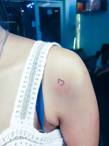 A simple heart outline in purple ink on the shoulder. This small tattoo is a sweet and personal expression of love.