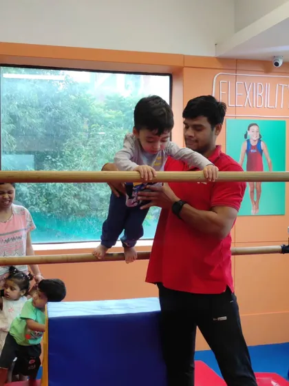 With a coach's steady hands, this toddler gains the confidence to balance and move across the bars, an important step in developing gross motor skills.