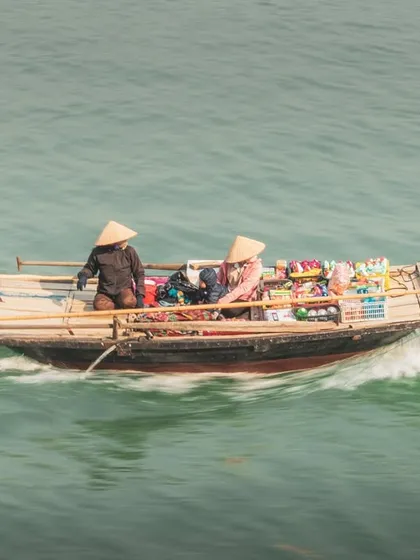 A panning shot of a floating shop in motion, its wake trailing behind as it navigates the waters of Halong Bay.