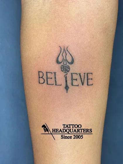 A minimalist "Believe" tattoo where the letter 'L' is creatively replaced with a Trishul, blending faith and self-belief.