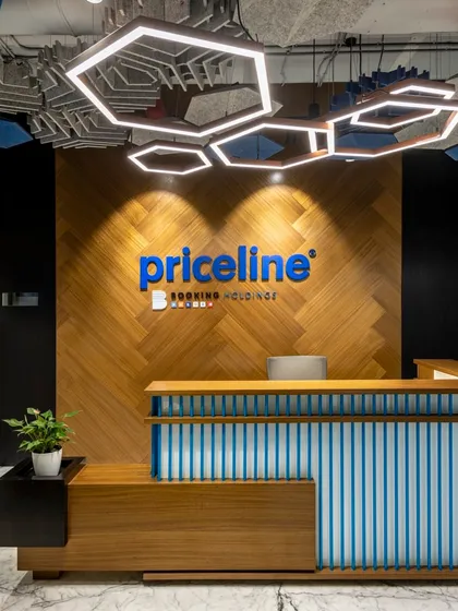 The reception area we designed for Priceline, a Booking Holdings company. The design features a custom reception desk, chevron wood paneling, and a striking hexagonal lighting fixture, creating a memorable and professional first impression.