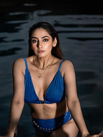 A captivating poolside portrait taken at dusk. The dark water and low light create a moody and intimate setting, perfect for a bold and confident look.