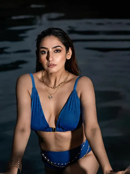 A captivating poolside portrait taken at dusk. The dark water and low light create a moody and intimate setting, perfect for a bold and confident look.