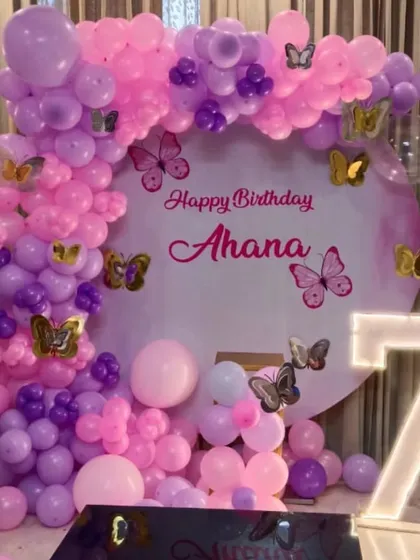 A butterfly-themed 7th birthday party. This decoration features a personalized circular backdrop, a pink and purple balloon arch, and a marquee number '7'.