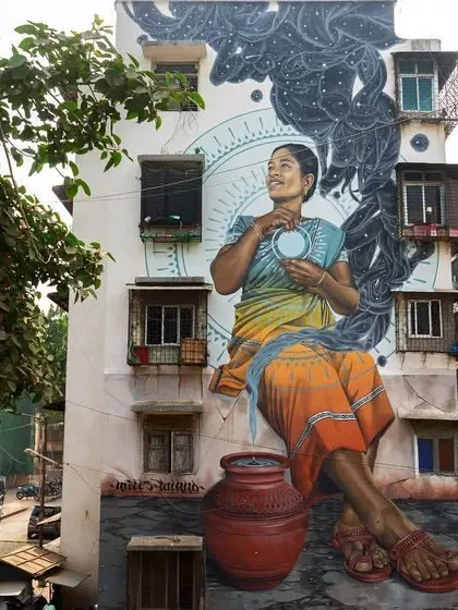 A woman in a colorful sari sits with a water pot, embodying the sunset. This mural by artist Miles Toland in the Mahim East art district was created to honor and reflect the local culture.
