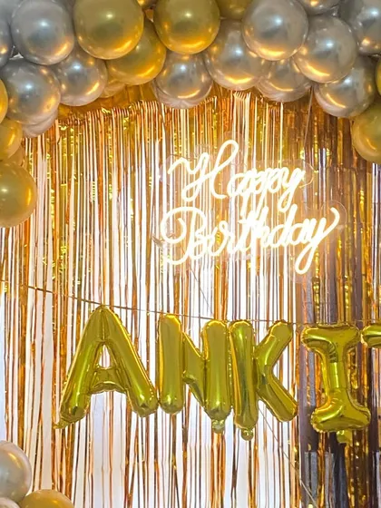 A glamorous gold-themed birthday backdrop. This setup features a shimmering gold foil curtain, a "Happy Birthday" neon sign, and the name "ANKIT" in large gold foil balloons, perfect for a milestone celebration.