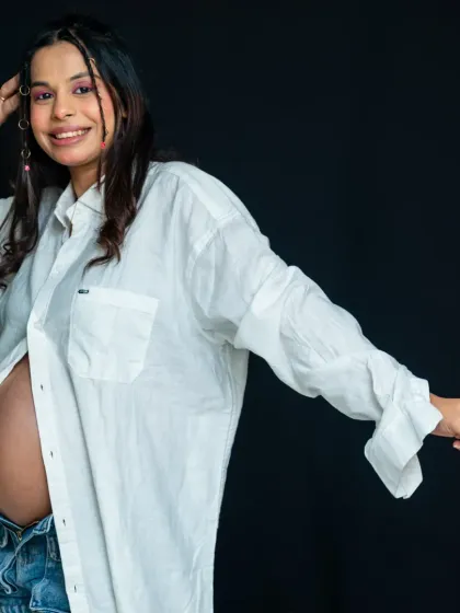 A confident and modern maternity portrait. The mom-to-be rocks a casual, unbuttoned white shirt and jeans, showing off her bump with style and attitude.