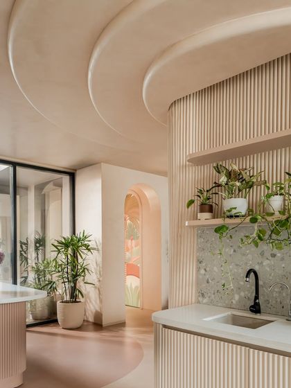 The kitchen bar area features a terrazzo countertop and fluted details, with open shelves for plants. The ceiling's curves are echoed here, creating a cohesive look that flows from the living room.
